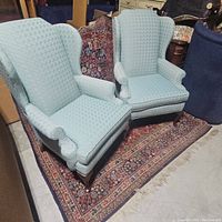 Pair of seafoam green wing back chairs on a patterned rug, viewed at an angle.