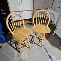 Two light natural wood swivel bar stools with spindle backs showing front and side views.