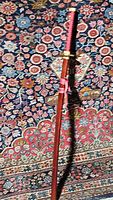 Full length photo of katana sword on floral rug, showing red sheath and tied pink cord.