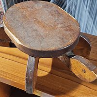 Side view of small wooden stool resembling a turtle, showing round seat and carved wooden legs
