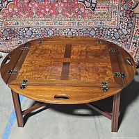 Front view of the vintage wooden coffee table with folding sides down, showing the warm wood grain finish and oval shape.
