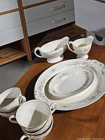Set of two oval trays, two gravy boats, and four tea cups showing floral and gold trimmed decoration on a wooden surface.