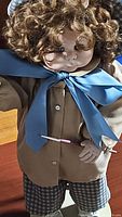 Curly-haired vintage doll wearing large blue satin bow and checkered shorts