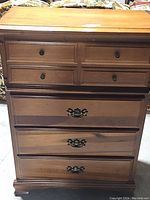 Front view of the wooden dresser showing four drawers with brass hardware and surface wear.