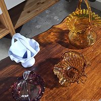 Four assorted vintage glass baskets on a wooden surface.