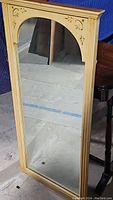Full view of rectangular mirror with light wood frame and carved arched top.