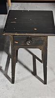 Front view of the black wooden table showing wear spots and round knob on single drawer
