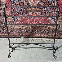 Front view of the entire wrought iron blanket rack against a patterned rug background.