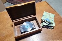 Wooden case with open lid showing the metal disk music box inside and three boxes of disks next to it.
