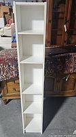 Front view of the narrow white bookcase with five shelves showing overall structure and condition.