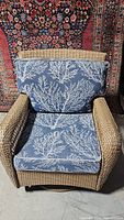 Front view of wicker swivel chair with blue cushions featuring white coral pattern, shows overall shape and cushion design.