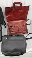 Photo showing three bags including a dark red leather briefcase, a dark red leather satchel with double buckles, and a black leather shoulder bag with zipper pocket.
