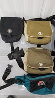 Three Crumpler shoulder camera bags, black, tan, and olive, all with flap covers and buckle closures