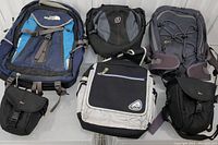 Seven assorted backpacks and camera bags including The North Face, Linx, MEC, and Lowepro arranged on white surface showing top fronts.