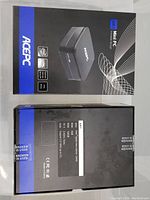 Top view of two ACEPC AK1 Mini PC boxes, showing front packaging and back with specifications and sealed stickers.