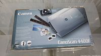 Box top view showing Canon CanoScan 4400 flatbed color image scanner with some photo slides and film strips depicted on packaging.