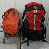 Front view of two backpacks side by side: Gregory Shasta (red/black) and Black Diamond Nitro (orange).