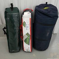 Three packed camping items lined up: dark blue Kelty Screenhouse 12 bag, middle Outbound 3P tent bag with visible label, green Outbound 3P tent bag.