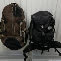 Photo showing two backpacks side by side: LifeVenture brown backpack on left, Black Diamond black backpack on right with waist belt visible.