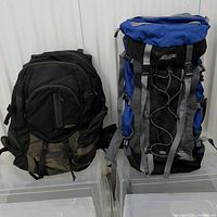 Two backpacks side by side. The left is black and grey MEC 65L, the right is blue and black Mountain Equipment Co-op Pangea 40L.