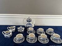 Full view of tea set displayed on a blue cloth, including teapot, sugar bowl, creamer, 4 cups and 4 saucers