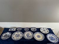 View of ten blue and white plates and dishes arranged on a dark blue cloth.