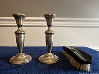 Pair of weighted sterling silver candle holders standing upright next to a brush with a silver decoration on a dark blue cloth.