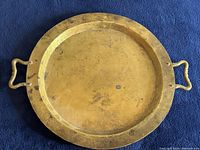 Top view of the brass tray showing round shape and two handles, highlighting surface wear and patina