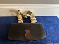 Overall view of the black leather bullet bag with beige strap against a blue background.