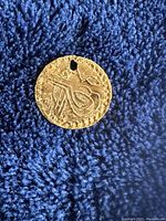 Obverse of coin showing stylized motif and punched hole, on blue cloth background