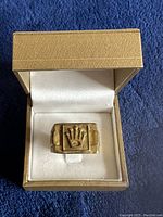 Front view of ring in presentation box showing rectangular top and crown emblem