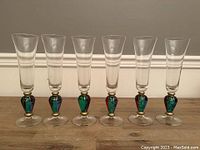 Six identical Bohemian Czech champagne flutes with clear glass tops and colorful, gold-accented stems, displayed in a row.