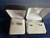 Two pairs of earrings in black boxes on blue surface, showing the size and differences in style.