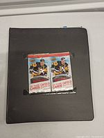 Two unopened sealed packs of 2016-2017 Tim Hortons hockey trading cards placed on a black binder (closed).