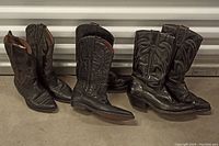 Three pairs of black cowboy boots of different styles and sizes placed side by side.