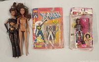 Two dolls and two boxed action figures and dolls laying on a flat surface