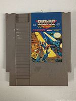 Front side of the gray NES cartridge showing colorful Bionic Commando label with Capcom logo and artwork.