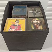 Black fabric cube filled with jewel case CDs including Queen, R.E.M., Rage Against Machine, Van Halen