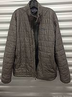 Brown Patagonia quilted jacket hanging on a plastic hanger, showing front view with zipper partially open.