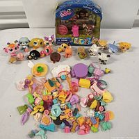 Wide view of 11 Littlest Pet Shop animal figures shown next to a large pile of assorted small plastic accessories, also includes one new-in-box packaged Littlest Pet Shop figure.
