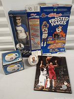 Full view of the collection showing the Ken Griffey Jr. doll in box, Frosted Flakes cereal box, baseballs in cases, loose baseball, and a basketball photograph.