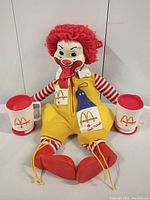 Front view showing Ronald McDonald plush doll holding the two mugs.