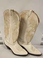 Side view of white leather cowboy boots showing intricate stitching and visible dirt wear.