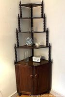 Full view of barley twist corner cabinet showing four graduated shelves and two-door cabinet base with wooden knobs and turned finials.