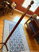 Oak coat stand shown standing in room with wood floor and chair nearby, highlighting brass hooks and four-legged base.