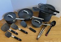 Cookware set showing pots, pans with lids, and various utensils laid out to display contents and condition.