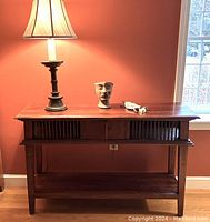 Full view of the console table with weighted lamp, terra cotta head, and miniature shield on top