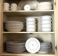 Shelves displaying stacks of white plates (dinner, salad, bread), bowls, and mugs, showing the quantity and all white color.