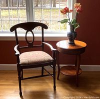 Wooden armchair with curved top rail, oval backrest, and paisley upholstered seat alongside round cherry wood side table.