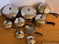 Full set of eight Farberware stainless steel saucepans and pots with matching lids and black handles arranged on the floor.